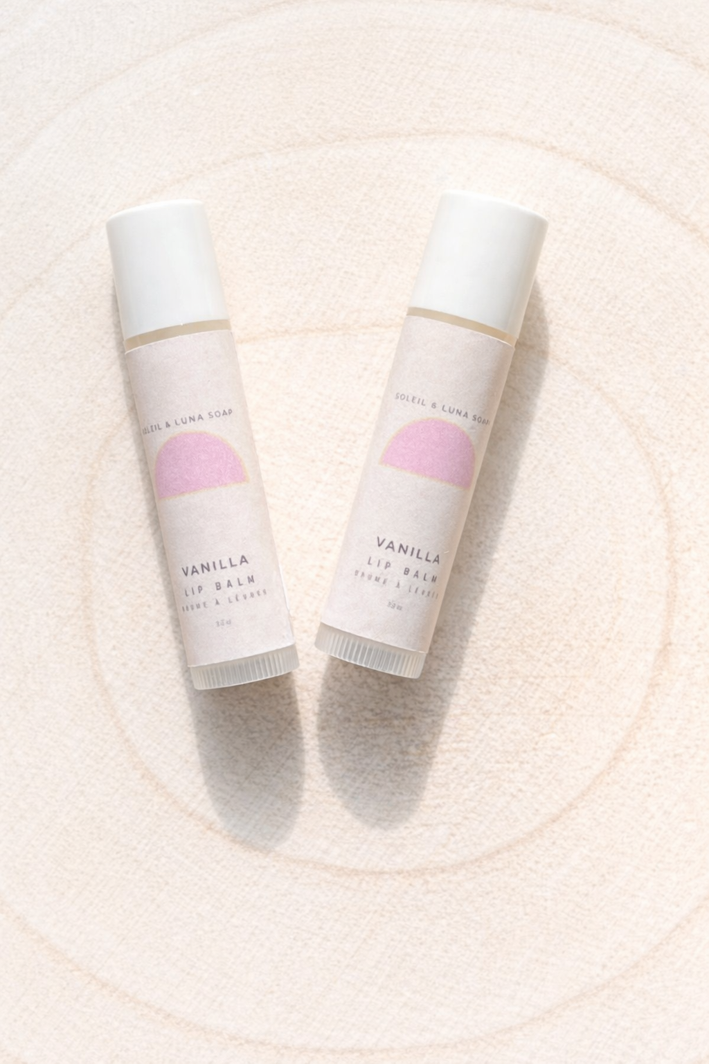 Two lip balm tubes with a pink label on a light beige background