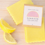 Yellow soap bar with a 'Sunriser' label on a wooden surface with lemon slices.