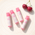 Four lip balms with pink caps and cherry flavor label on a light background with cherries.