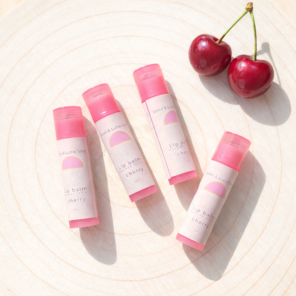 Four lip balms with pink caps and cherry flavor label on a light background with cherries.