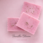 Pink soap bars with heather flowers on top of a pink background, labeled 'Vanilla Bloom' and 'rose scented'.