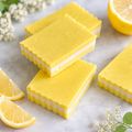 Yellow soap bars with white centers on a marble surface with lemon slices and flowers.