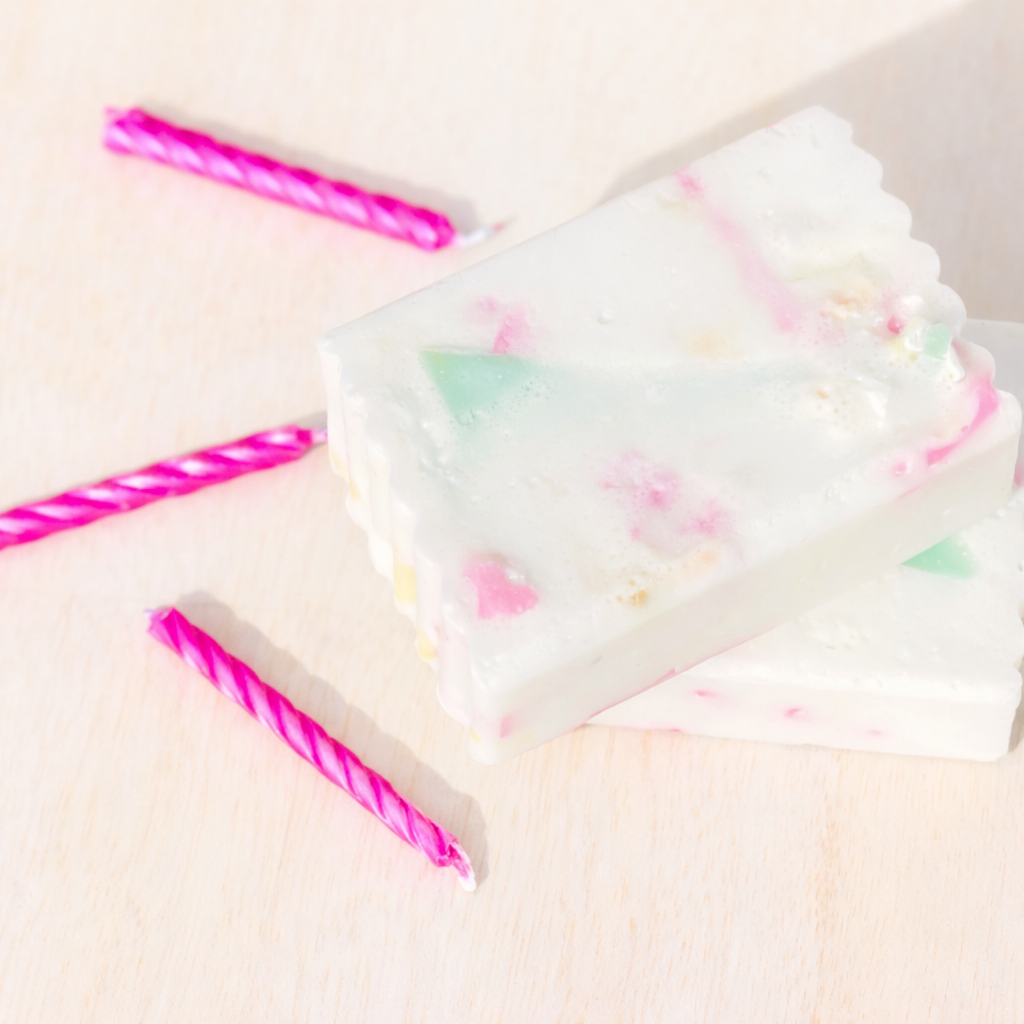 White soap with colourful soap scrap pieces on a light pink background with pink striped candles