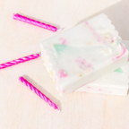 White soap with colourful soap scrap pieces on a light pink background with pink striped candles