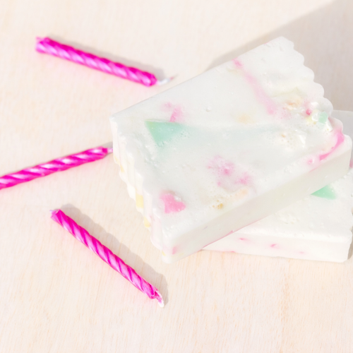 White soap with colourful soap scrap pieces on a light pink background with pink striped candles